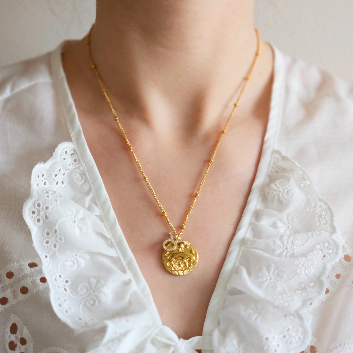 Złoty naszyjnik ZODIAC Byk z monetą i małą zawieszką ozdobioną cyrkoniami prezentowany na dekolcie